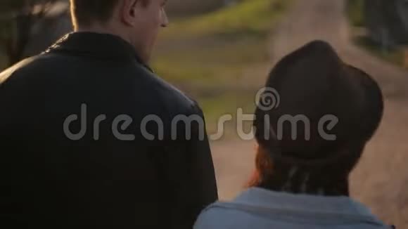 一对年轻夫妇牵着手慈爱地微笑着走在秋天的公园里中弹后景视频的预览图
