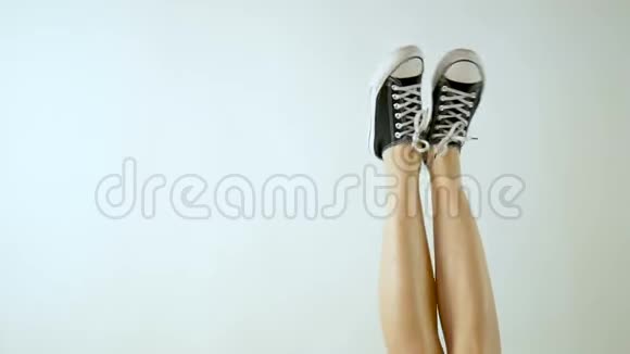 经典黑白运动鞋中的女性腿腿是上升和倾斜从侧面到侧面灰色背景视频的预览图