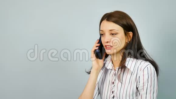 戴着深色长发的微笑女商人在手机上聊天穿衬衫的年轻女子谈蓝色智能手机视频的预览图