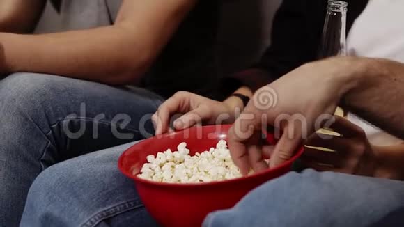 特写一碗红爆米花和一瓶啤酒或苏打水在腿上的场景双手抓着碗里的爆米花视频的预览图