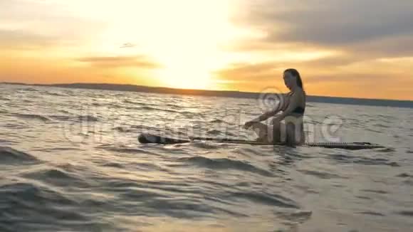 女人坐在海里的冲浪板上视频的预览图