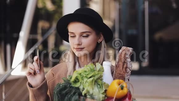 年轻漂亮的女人穿着时髦的外套站在街上拿着一包产品拿着信用卡视频的预览图