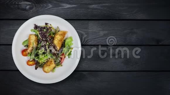 沙拉与三文鱼在面包屑与生菜和芝麻在黑色木制背景上旋转顶部景观视频的预览图