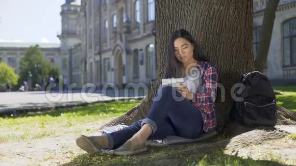 亚洲女孩坐在树下在笔记本上写得很快灵感诗歌视频的预览图