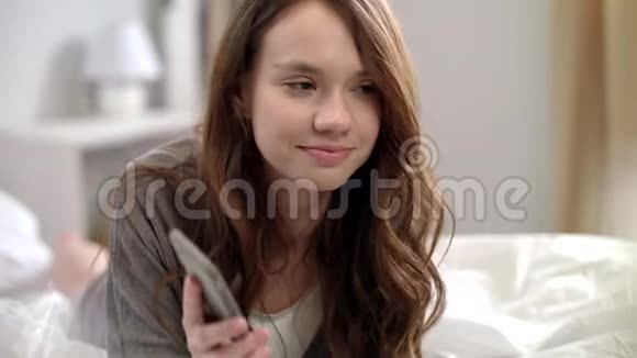 年轻的女人在床上用手机说话微笑的女人在打电话视频的预览图