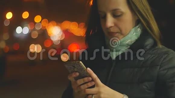 年轻漂亮的女人晚上在街上使用智能手机慢动作视频的预览图