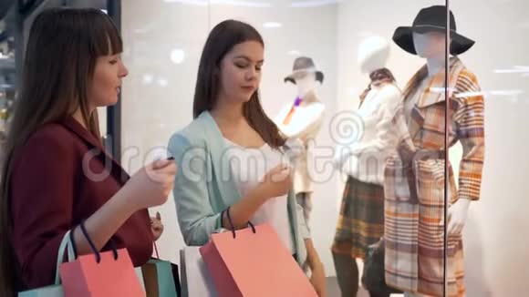 购物狂的女朋友带着袋子站在商店橱窗附近收集新的衣服并讨论在商场购物视频的预览图