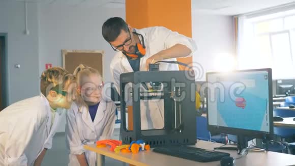 孩子们和一位学校老师在实验室里用一台3D打印机工作关闭视频的预览图