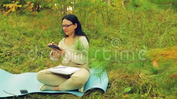 一个戴眼镜的女人在森林的边缘用平板电脑工作视频的预览图