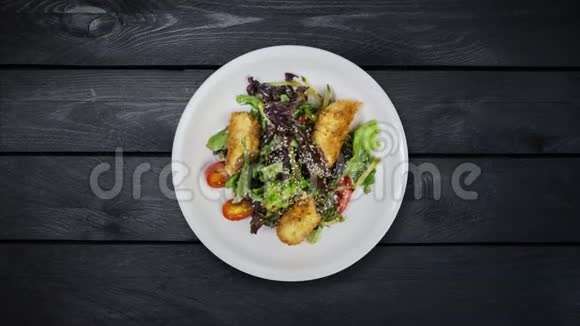 沙拉与三文鱼在面包屑与生菜和芝麻在黑色木制背景上旋转顶部视图视频的预览图