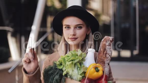 年轻漂亮的女人穿着时髦的外套站在街上拿着一包产品拿着信用卡视频的预览图
