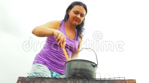 一个女人在火上用木勺在水壶里搅拌汤特写镜头视频的预览图