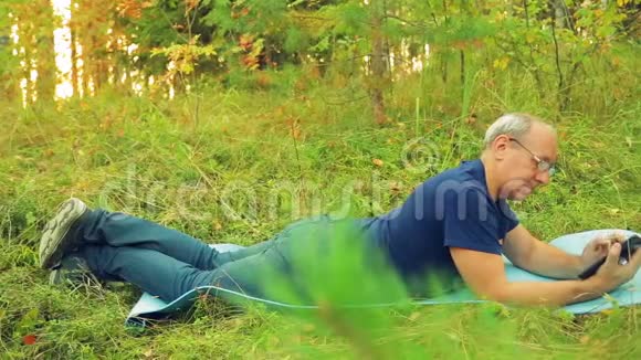 一个戴眼镜的人躺在草地上做瑜伽的地毯上在平板电脑上用信使传达信息视频的预览图