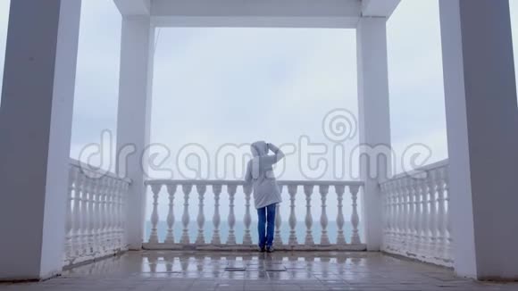 穿着白色夹克的女人在美丽的露台上欣赏海景后景视频的预览图