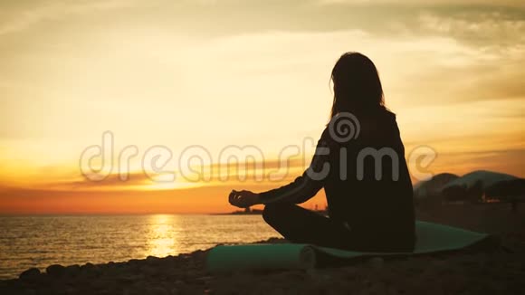 日落时分年轻美丽健康的女子在海边的莲花位置冥想的剪影年轻女子练习视频的预览图