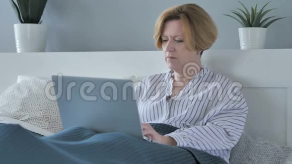 兴奋的老年妇女躺在床上在线视频聊天视频的预览图