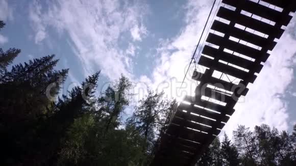 悬索桥上人的底视图库存录像人走在云杉背景下的木制吊桥上视频的预览图