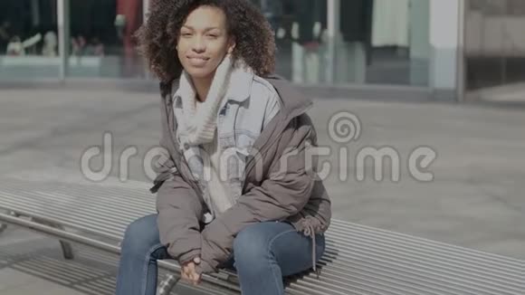 在城市街坐在长凳上的一个留着非洲发型的漂亮女孩视频的预览图