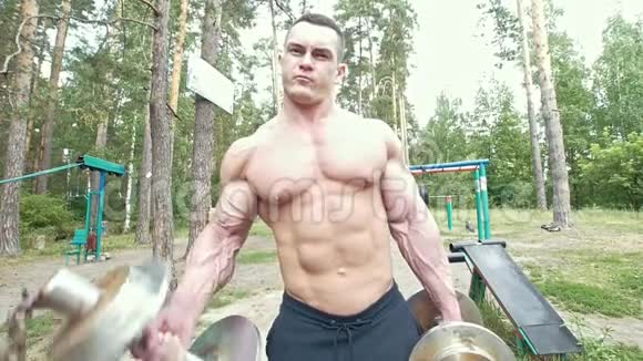 一个肌肉发达的年轻人在森林里拿起沉重的哑铃视频的预览图