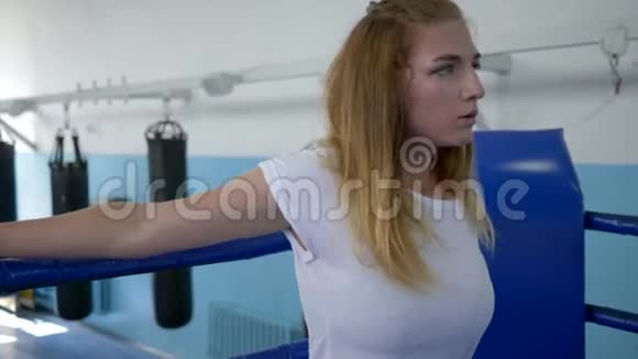 女运动员在经过艰苦的锻炼后休息在健身房里站在拳击场上喝着瓶子里的水视频的预览图