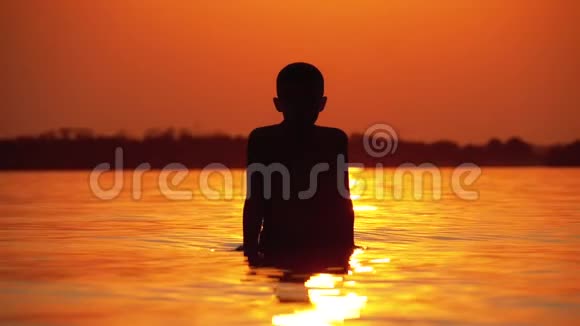 日落时分男孩的剪影举起双手创造水的飞溅慢动作视频的预览图
