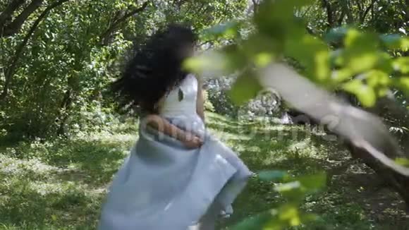 穿着蓝色连衣裙的美丽黑发少女在花园里慢悠悠地走着视频的预览图