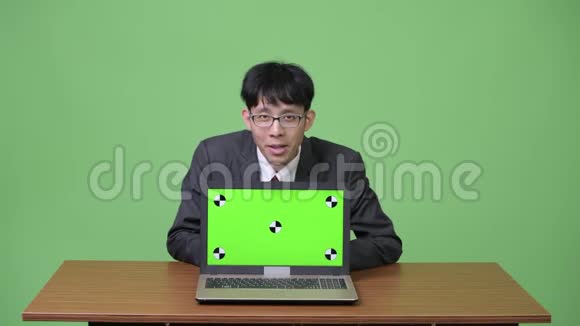 年轻快乐的亚洲商人一边说话一边把手提电脑对着镜头看视频的预览图