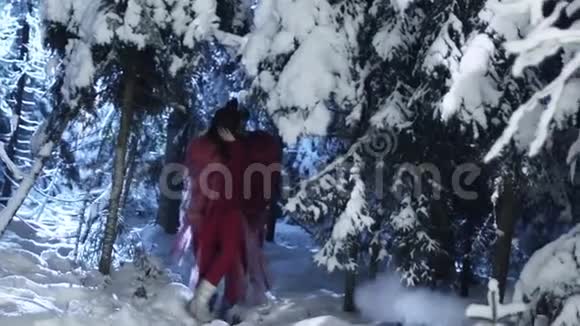 可爱的男女穿着红色的衣服在白雪皑皑的冬林中慢慢移动视频的预览图