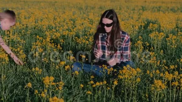男孩送给妈妈一束野花亲吻她坐在黄花丛中的草地视频的预览图