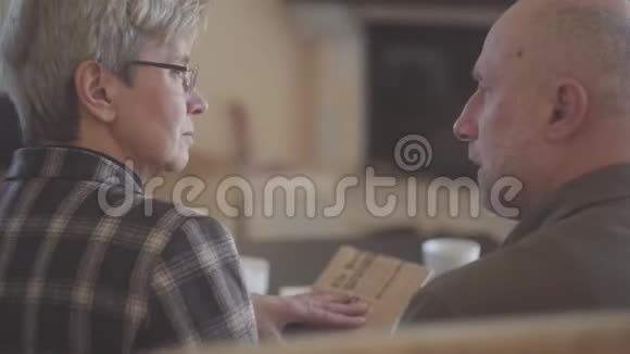 老夫妇男人和女人坐在沙发上拿着一本书互相交谈和微笑家庭关系视频的预览图