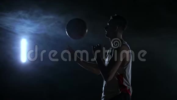 近镜头篮球运动员旋转球在他的手指黑暗的雾室与泛光灯视频的预览图