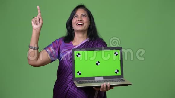 成熟快乐美丽的印度女人一边看着笔记本电脑一边指着视频的预览图