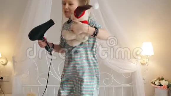 一位爱玩的年轻女士在吹干机里唱歌在床上跳舞和跳跃听音乐视频的预览图