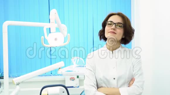 美丽的年轻女子牙科医生的肖像交叉在牙科诊所的橱柜自信的医生视频的预览图