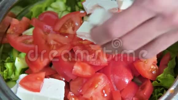 在希腊纯素番茄沙拉上加入橄榄和生菜叶用女性主厨的手将Feta奶酪立方体这就是视频的预览图