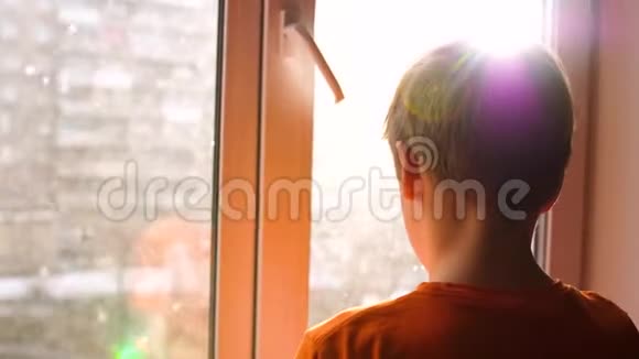 阳光明媚的冬天白天一个年轻人站在窗户旁边看着飘落的雪视频的预览图