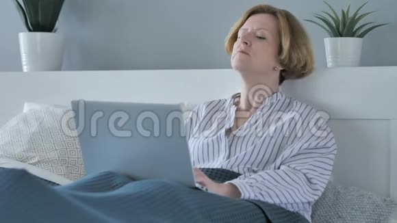 老年妇女在床上放松时在笔记本电脑上工作视频的预览图