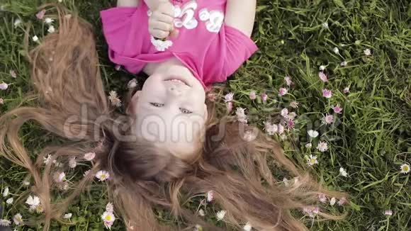 特写微笑的小可爱小女孩躺在绿草上捧着鲜花看着镜头视频的预览图