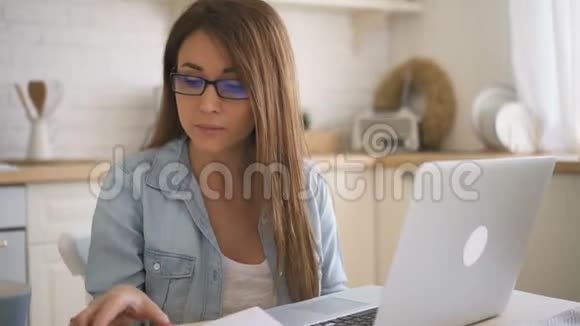 戴着眼镜穿着蓝色衬衫的年轻女子在笔记本电脑上工作享受着她的交流视频的预览图