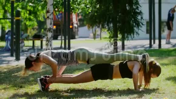 运动女孩在公园里做举重俯卧撑她的朋友躺在上面视频的预览图
