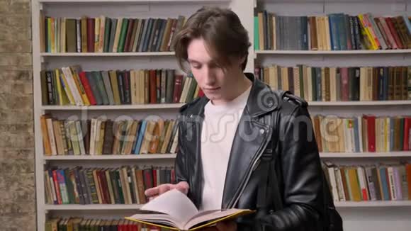 年轻英俊的学生站在图书馆拿着书对着镜头微笑书架背景视频的预览图