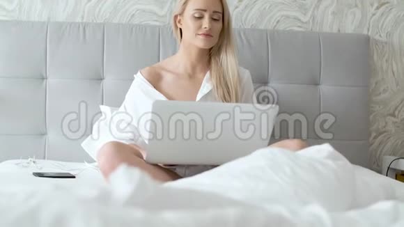 穿着优雅白衬衫手提电脑坐在床上的女人视频的预览图