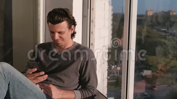 男人在手机上看视频日落时坐在阳台上视频的预览图