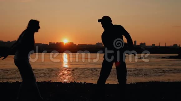 年轻幸福的一家人爸爸妈妈和宝宝在日落时分在河边玩耍剪影日落视频的预览图