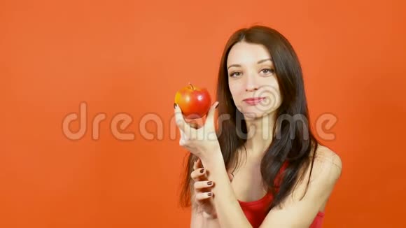 年轻美丽的女人完美的皮肤吃红苹果在橙色背景减肥理念健康食品视频的预览图