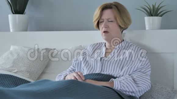 生病的老年妇女坐在床上咳嗽视频的预览图