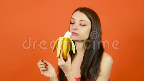 年轻健康的女人完美的皮肤吃香蕉在明亮的橙色背景热带水果素食视频的预览图