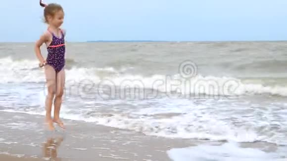 4K一个穿着泳衣的小女孩在海边玩海浪在海上一场微弱的风暴强大的风浪视频的预览图