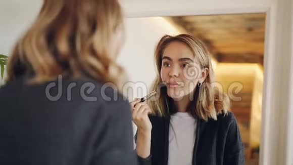 迷人的年轻女子正在镜子里用刷子和装饰化妆品化妆脸面视频的预览图