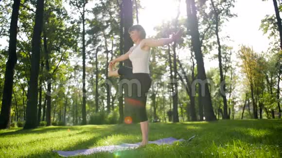 阳光明媚的夏日中年微笑妇女在公共公园练习瑜伽的4K慢动作镜头身体的概念视频的预览图